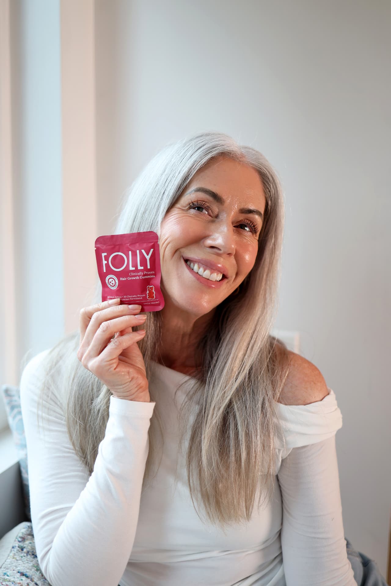 Creator holding a Folly Hair Growth Gummies sachet at home